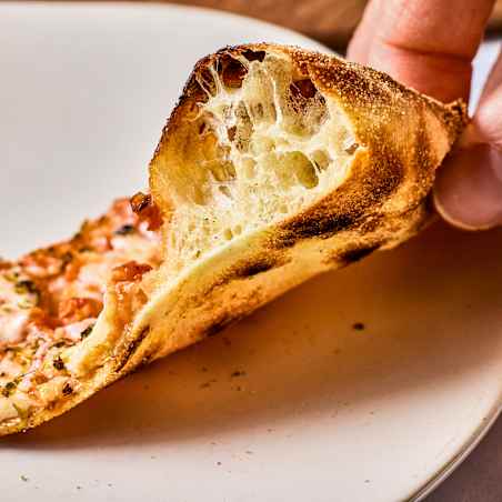 Person using their hand to show the airy, bubbly interior of a pizza crust.
